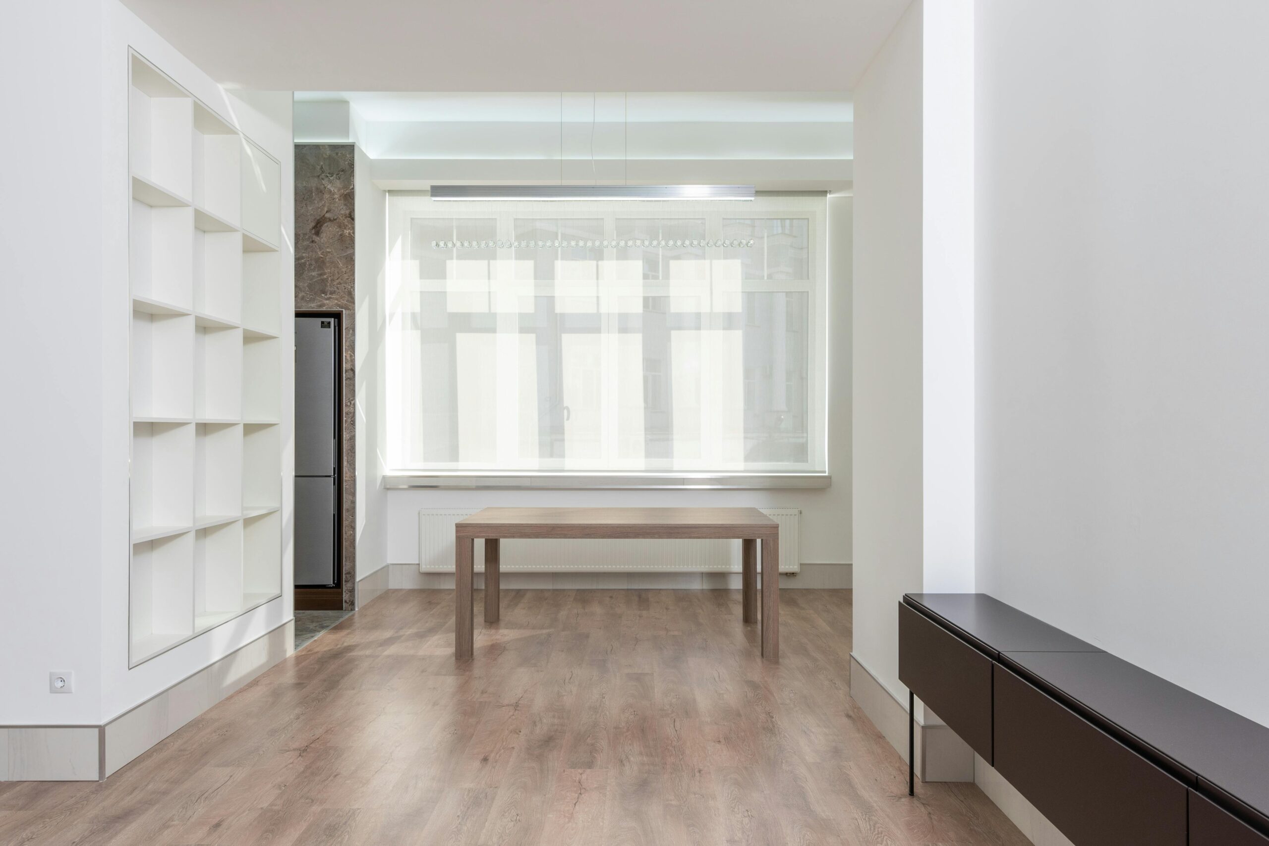 Bright minimalist living room interior with wooden flooring and simple furniture.